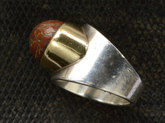 thumbnail of Side view of fossilized red jasper cabochon set in gold bezel on silver shank, shown on dark textured background.