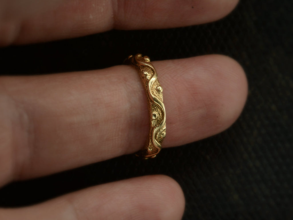 A vintage 18K yellow gold band patterned with a wave and dot pattern in high relief.  Shown on finger.