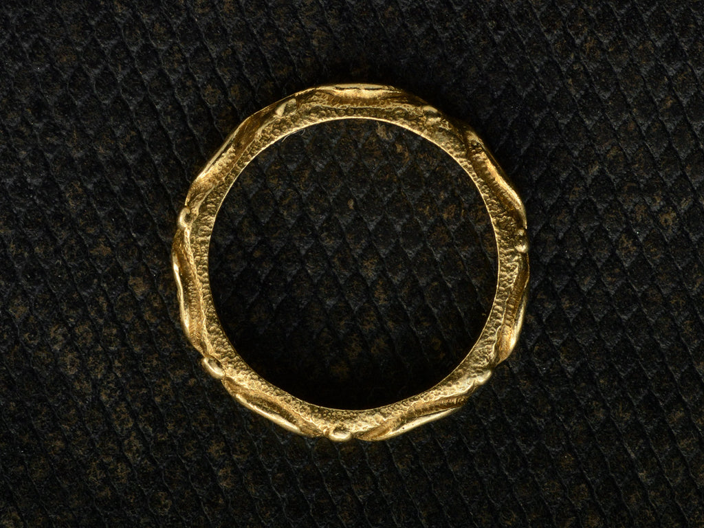 Side profile of a vintage 18K yellow gold band patterned with a wave and dot pattern in high relief, shown on dark textured background.