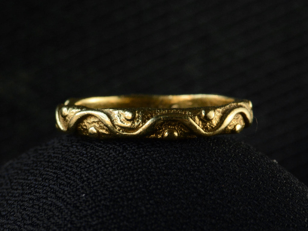 A vintage 18K yellow gold band patterned with a wave and dot pattern in high relief, shown on dark background.