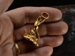 thumbnail of Front vew of antique gold watch fob with a nude women resting on a base of vines, flowers and flowing water.  Shown on hand.