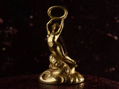 thumbnail of Front view of antique gold watch fob with a nude women resting on a base of vines, flowers and flowing water.  Shown on dark background.