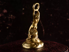 thumbnail of Back right view of antique gold watch fob with a nude women resting on a base of vines, flowers and flowing water.  Shown on dark background.
