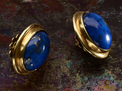 thumbnail of Angled view of a pair of oval blue lapis lazuli stud earrings in 18k yellow gold, shown on dark background.