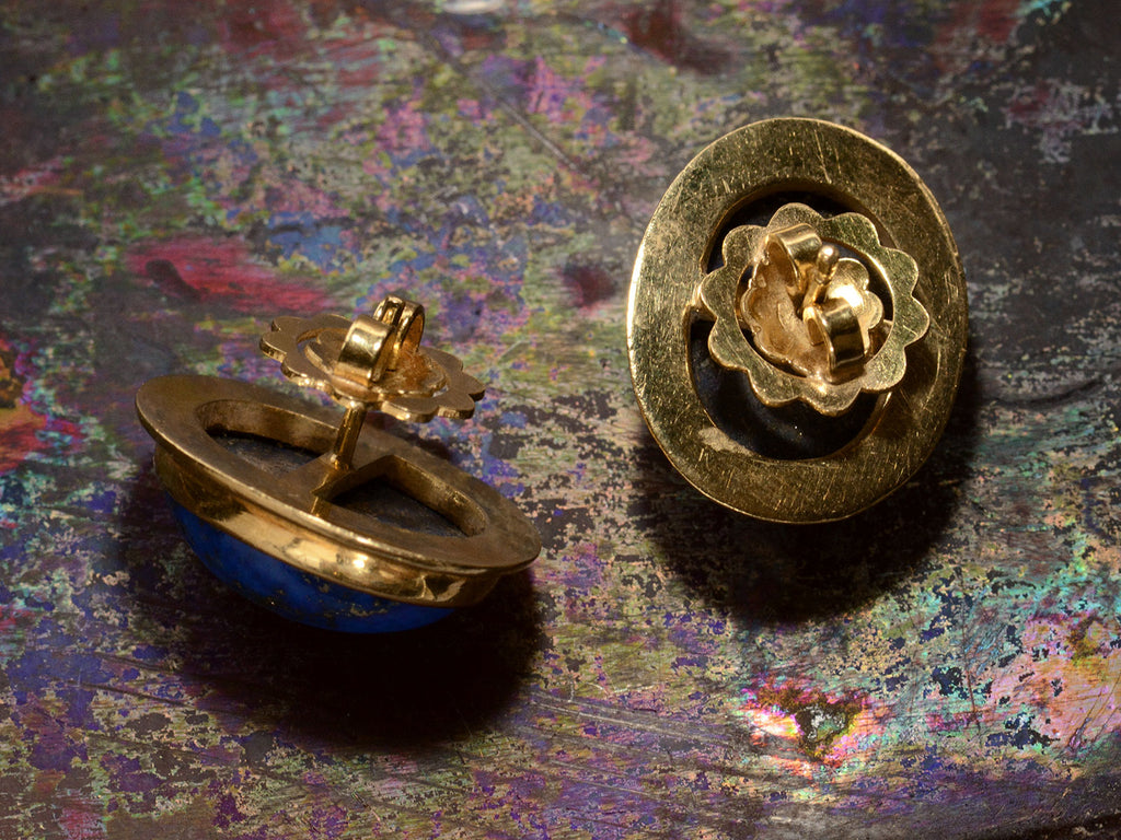 Reverse sides of oval blue lapis lazuli stud earrings in 18k yellow gold, shown on dark background.