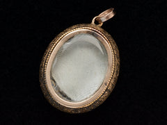 thumbnail of Backside view of oval antique gold locket with shown glass compartment with gray silk beneath it, shown on dark background.