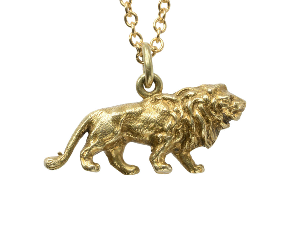 Detail view of a detailed antique gold lion charm, hanging on cable chain. Shown on white background.
