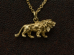 thumbnail of Detail view of a detailed antique gold lion charm, hanging on cable chain. Shown on dark textured background.