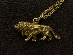 thumbnail of Opposite side of a detailed antique gold lion charm, hanging on cable chain. Shown on dark textured background.