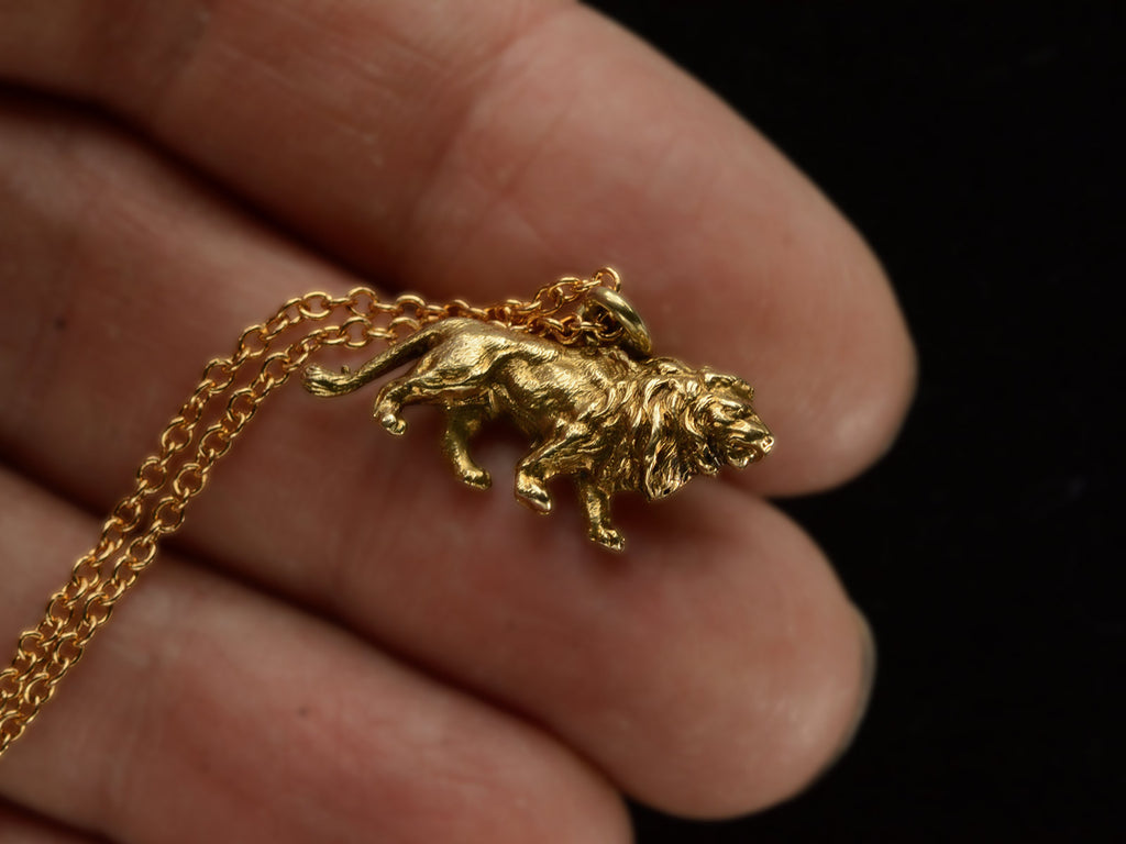 A detailed antique gold lion charm, hanging on cable chain. Shown on hand