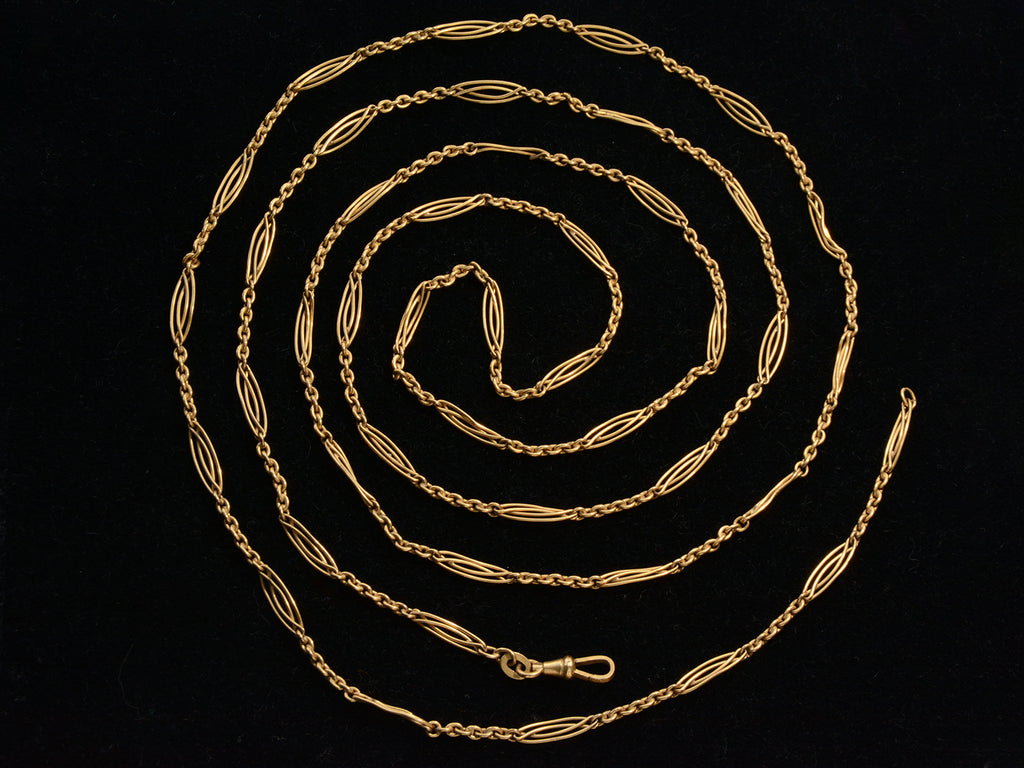 A long filigreed yellow gold plated c1890 chain, shown spiraled on a black background.