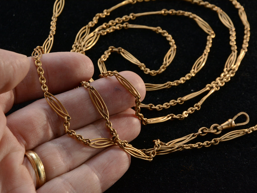 A long filigreed yellow gold plated c1890 chain, shown on a hand for scale.