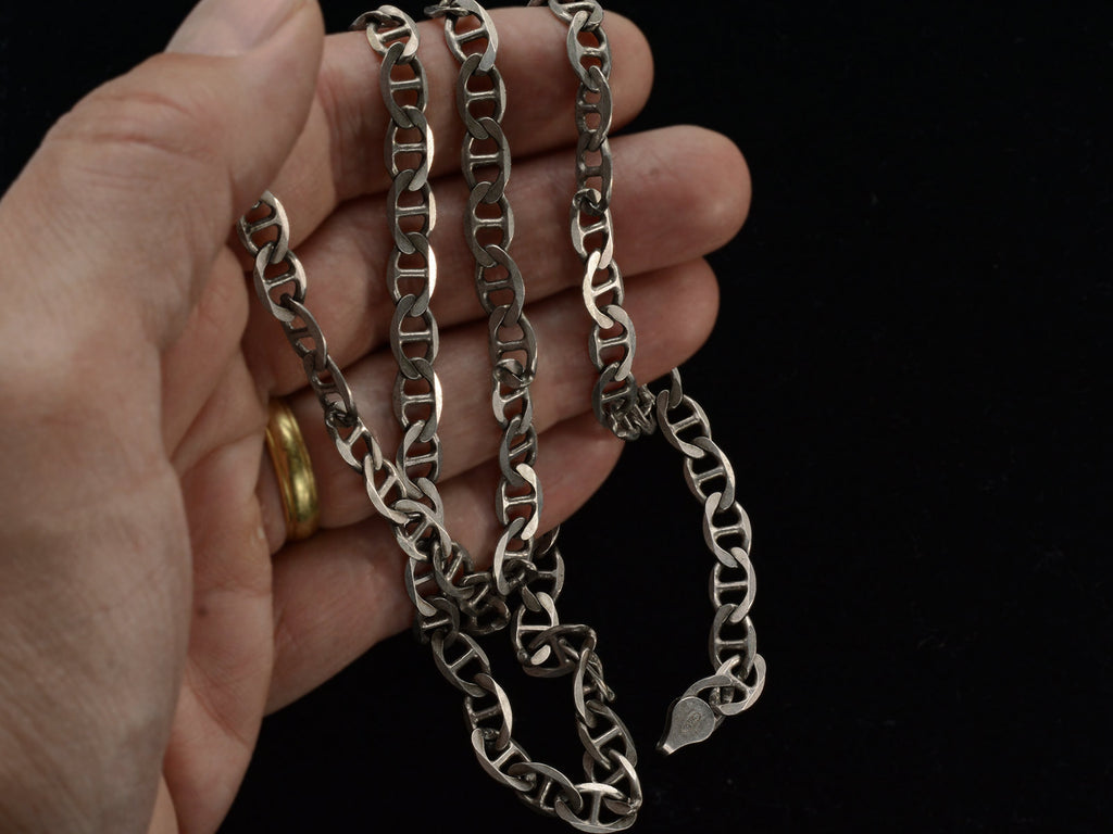 Hand holding a silver mariner link chain against a black background