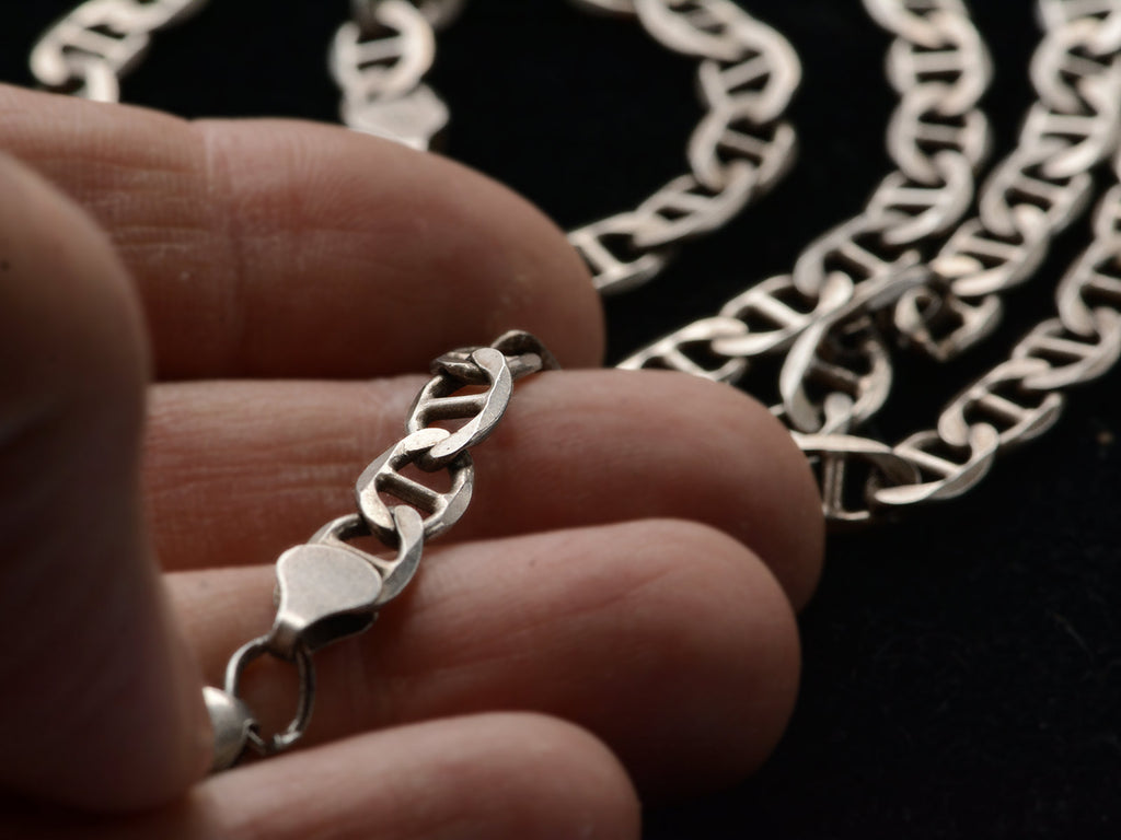 Close-up of a silver mariner link chain necklace held between fingers with a blurred background