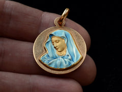 thumbnail of A vintage 18K yellow gold medal with the image of the Virgin Mary in blue enamel, on hand.