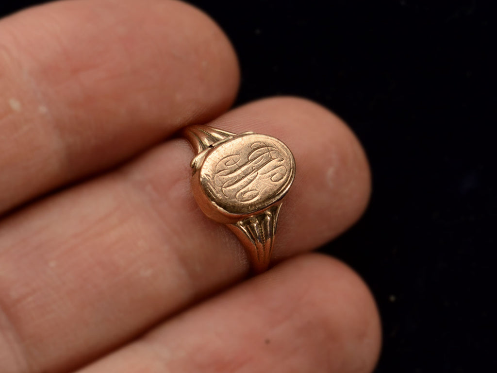 Front view of a c1920 antique signet ring shown with the locket closed and an indecipherable script monogram carved on the face of the signet. Shown on finger.