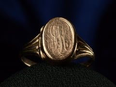 thumbnail of Front view of a c1920 antique signet ring shown with the locket closed and an indecipherable script monogram carved on the face of the signet. Shown on dark background.