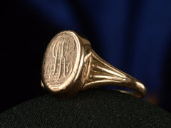 thumbnail of Angled view of a c1920 antique signet ring shown with the locket closed and an indecipherable script monogram carved on the face of the signet. Shown on dark background.