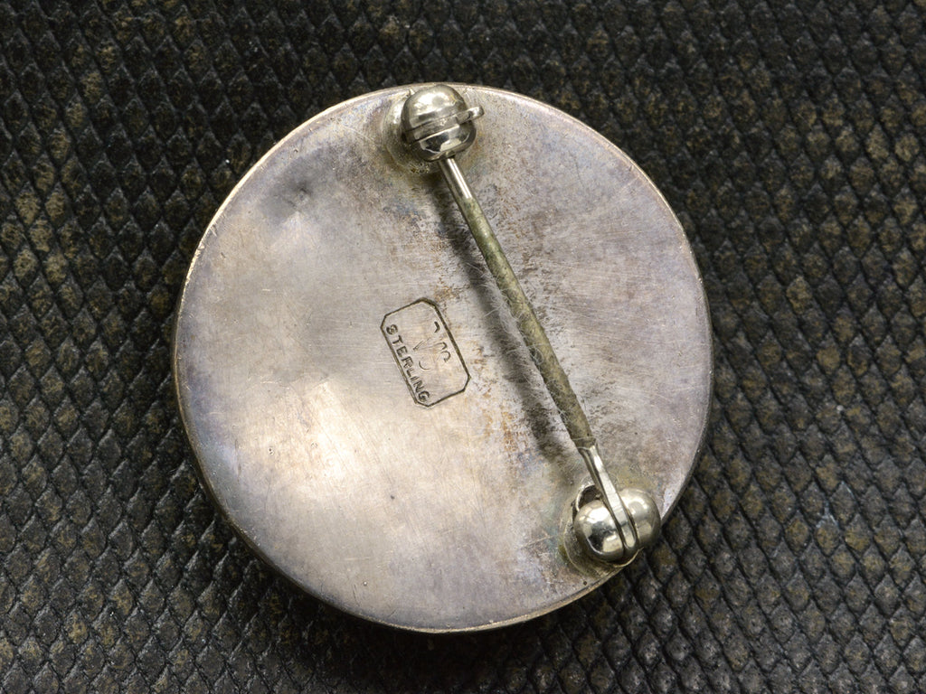 Reverse side of silver brooch showing pin fittings and a stamp with the letters "VS" and "STERLING"