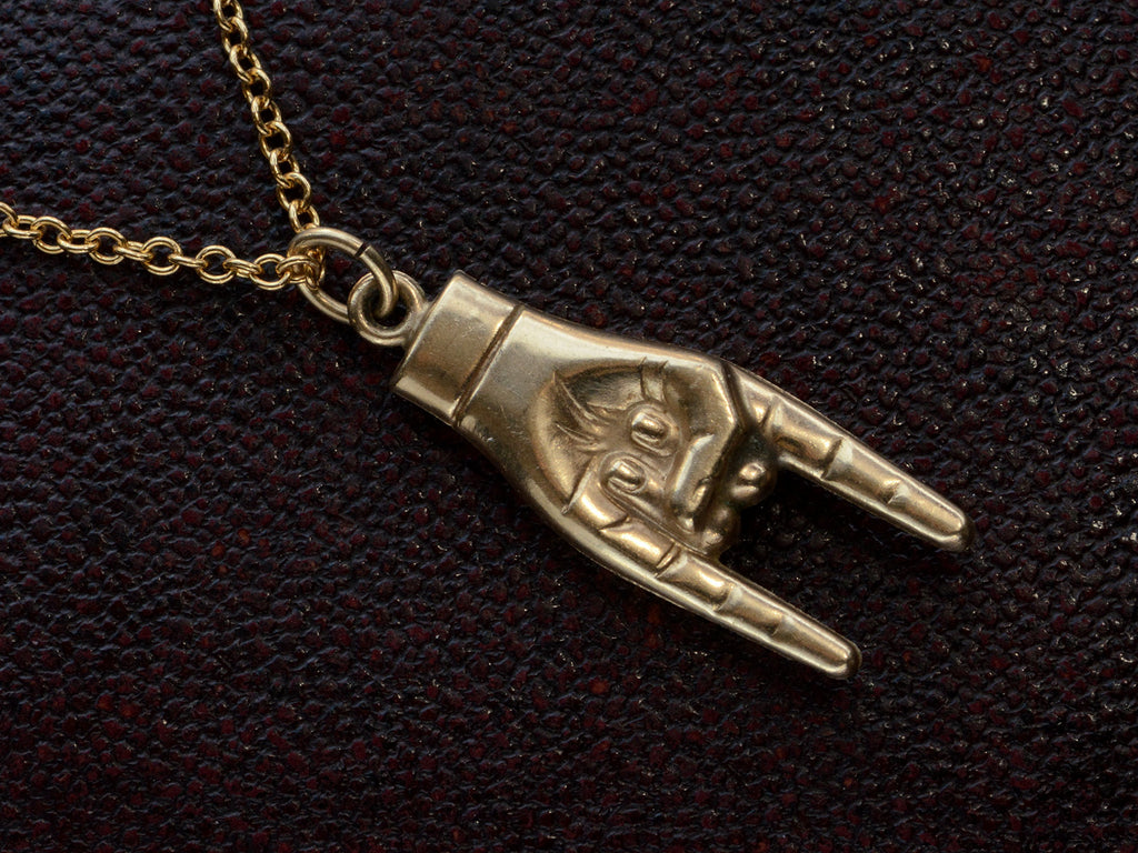 Detail of vintage gold hand pendant gesturing the sign of the horns, on dark textured background.