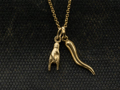 thumbnail of Detail of vintage 18K Italian charms, one of a hand gesturing the sign of the horns, the other of a cornicello horn, hanging together of cable chain. Shown on dark textured background.