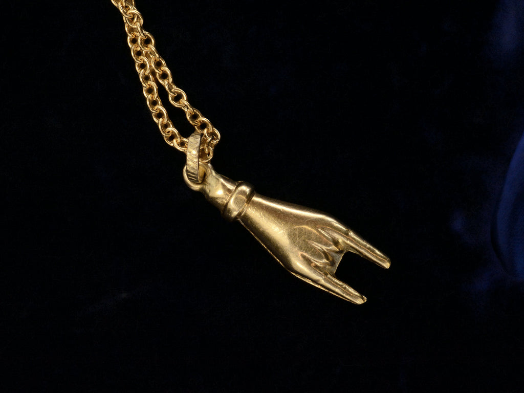 Opposite side of c1980 yellow gold hand charm gesturing the sign of the horns, shown on black background.
