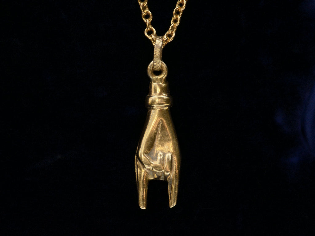 A c1980 yellow gold hand charm gesturing the sign of the horns, shown on black background.