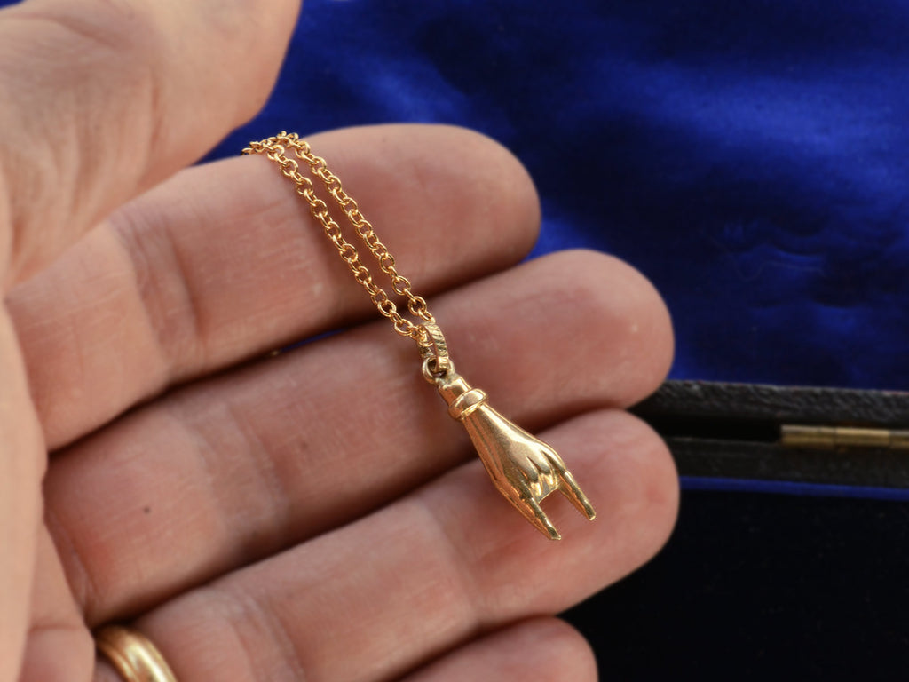 A c1980 yellow gold hand charm gesturing the sign of the horns, shown held in hand for scale.