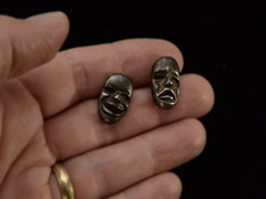 thumbnail of A pair of oxidized silver theatrical mask stud earrings depicting tragedy and comedy. On hand for scale.