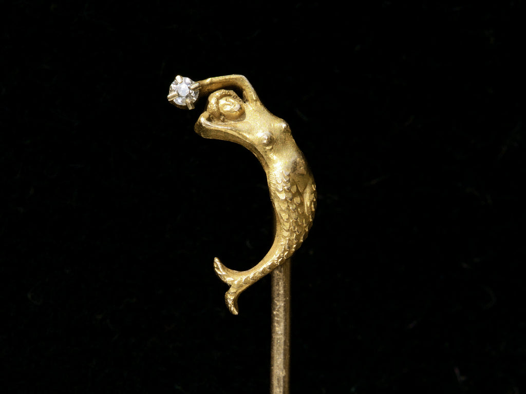 Detail of c1890 Yellow Gold Mermaid Stick Pin with a diamond, shown on black background.