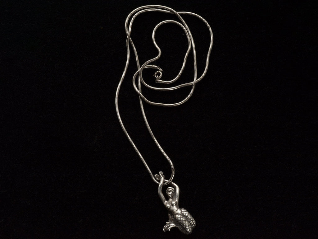 A vintage silver mermaid pendant on snake chain, on black background.