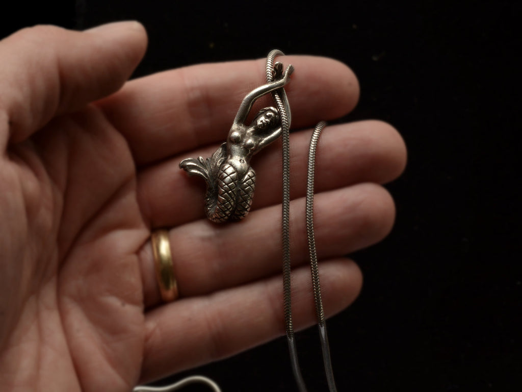 Detail of vintage silver mermaid pendant on snake chain, held in hand.