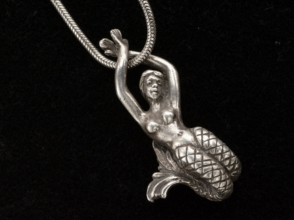 Detail of vintage silver mermaid pendant on snake chain, on black background.