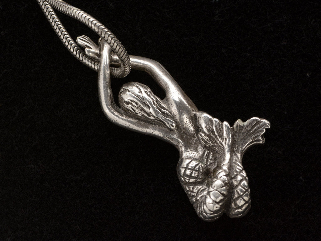 Reverse side of vintage silver mermaid pendant on snake chain, on black background.