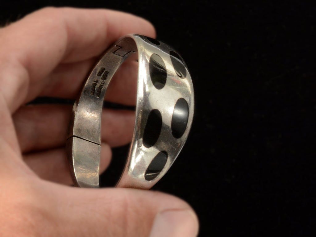 A hand holding a polished silver bracelet with large black oval inlays, set against a solid black background.