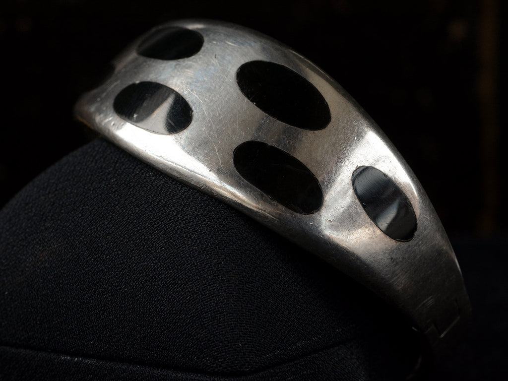 Angled view of a vintage silver bracelet with inset oval black onyx polka-dots, shown on black background