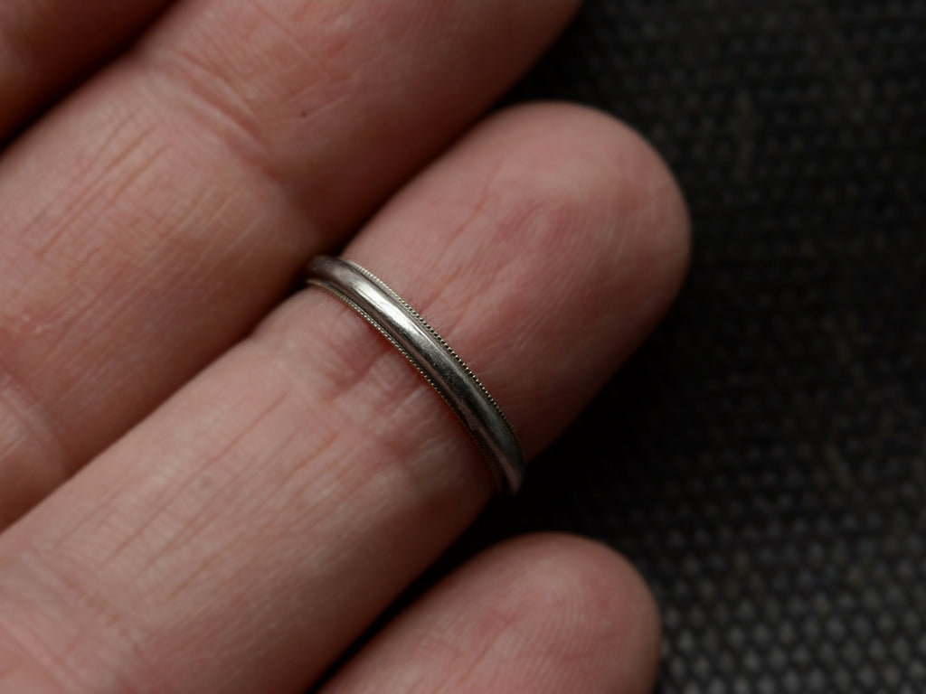 A 14K white gold c1940 wedding band with milgrain edges, shown on finger