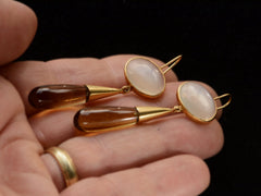 thumbnail of Pair of 18K yellow gold earrings with oval moonstone tops and amber-colored quartz teardrop pendants, shown on hand.