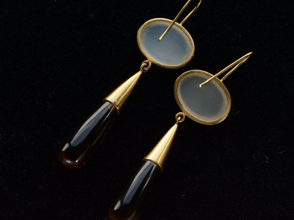 Reverse sides of 18K yellow gold earrings with oval moonstone tops and amber-colored quartz teardrop pendants, shown on dark background.
