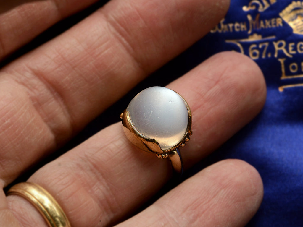 Vintage gold ring with silvery blue moonstone orb, shown on finger.