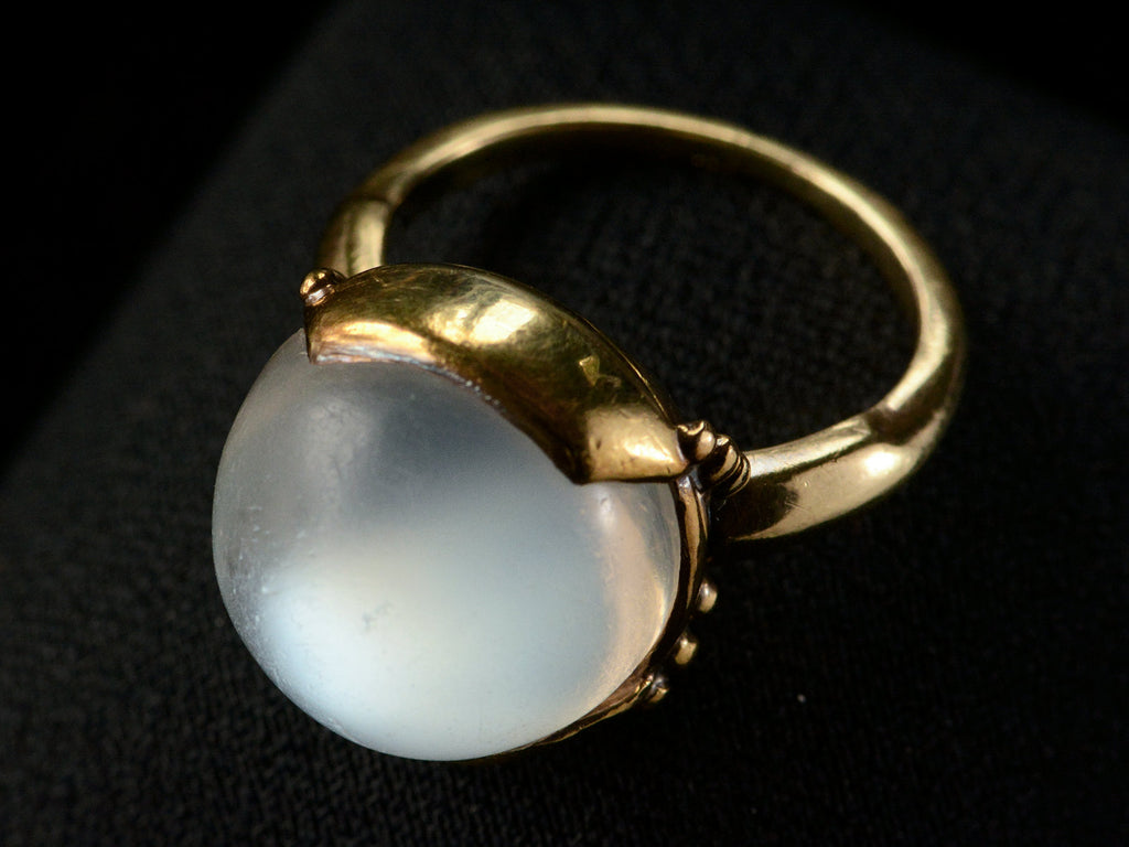 Elevated angled view of vintage gold ring with silvery blue moonstone orb, shown on dark background.