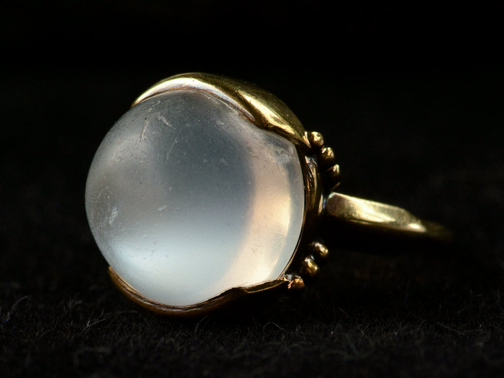 Right side view of vintage gold ring with silvery blue moonstone orb, shown on dark background.