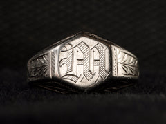 thumbnail of Front view of white gold Art Deco signet ring with a hexagonal top carved with a gothic script letter "M" and carved decorations on the sides, shown on black background.