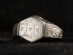 thumbnail of Angled view of white gold Art Deco signet ring with a hexagonal top carved with a gothic script letter "M" and carved decorations on the sides, shown on dark background.