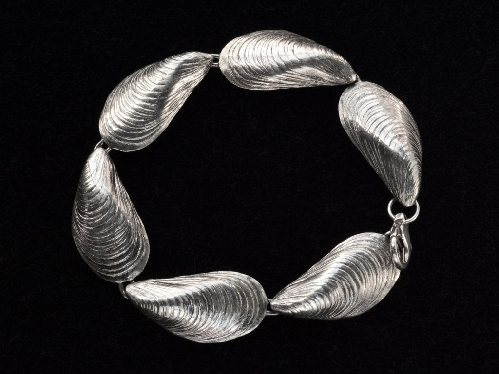 Silver bracelet with mussel shell links, on black background. Shown laid in a circle