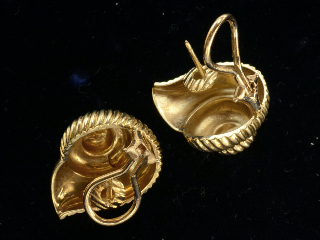 Reverse side of of yellow gold ammonite shaped earrings, showing posts and omega backs, on dark background.