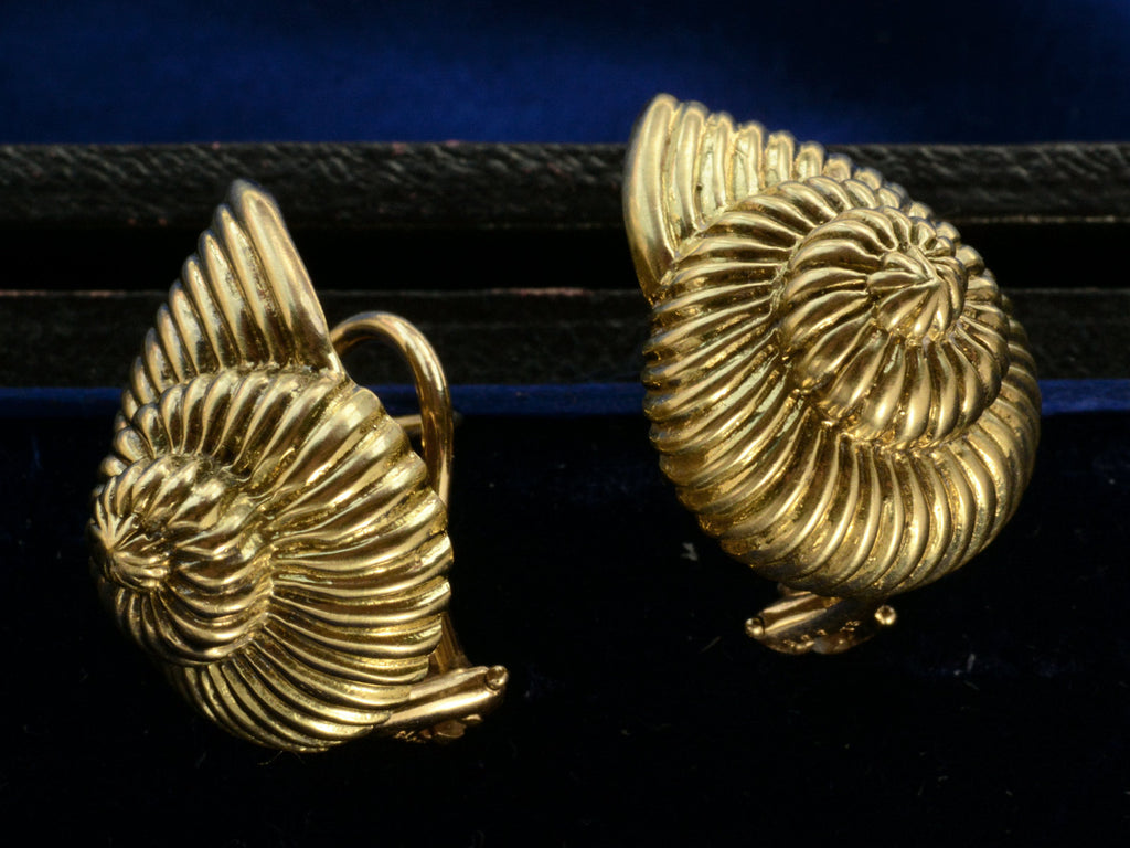 Angled view of pair of yellow gold ammonite shaped earrings, shown on dark background.