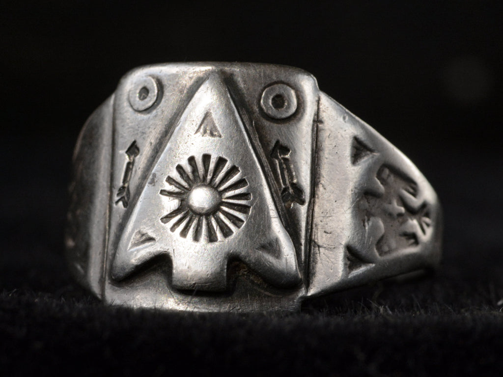 Angled front view of c1930 Navajo silver signet ring with an arrowhead design and eagles stamped on the shoulders, shown on dark background.