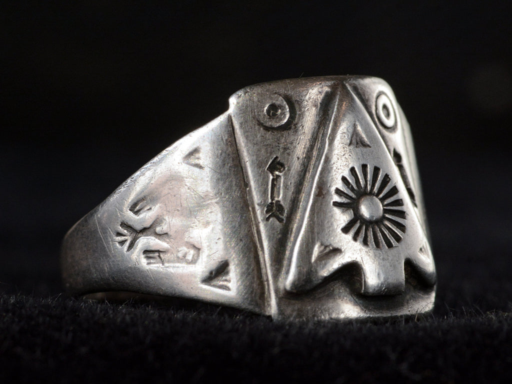 Side view of c1930 Navajo silver signet ring with an arrowhead design and eagles stamped on the shoulders, shown on dark background.