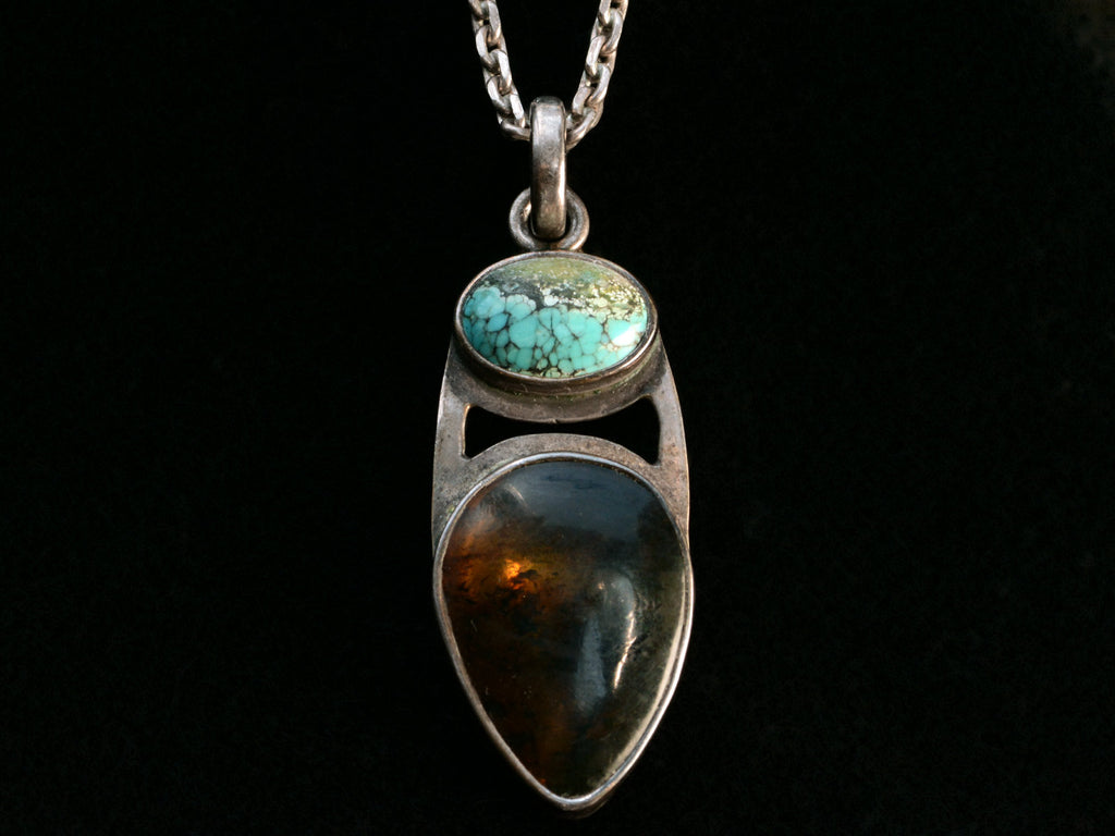 Silver pendant with oval turquoise and pear shaped tortoiseshell on black background.